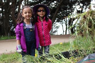 Two young girls by a bag full of weeds